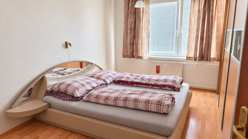 Schlafzimmer in einer 3-Zimmer-Wohnung mit Bett, Schrank unter dem Spiegel und Boden mit Holzdekor.