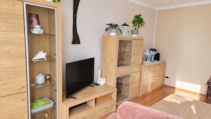 Wohnzimmer mit Holzmöbeln, dekorativen Blumen und einem Boden mit Holzdekor.
