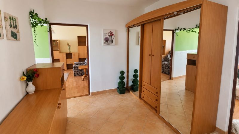 Ein Flur in einer 3-Zimmer-Wohnung mit Holzschränken und Dekorationen auf beigen Fliesen.