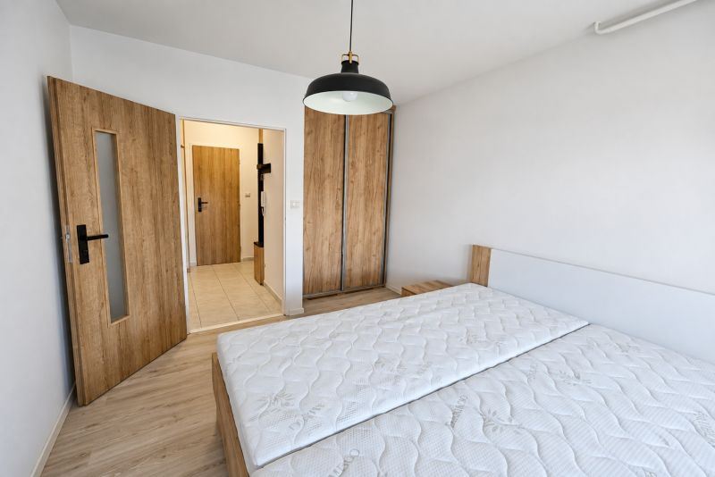 Schlafzimmer in einer 2-Zimmer-Wohnung mit Bett, Schrank und Boden in Holzoptik.