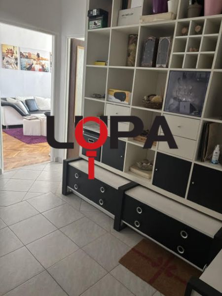 Der Flur in einer 2-Zimmer-Wohnung mit Fliesenboden und eingebautem Regal.