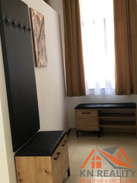 Flur in einer 2-Zimmer-Wohnung mit Bänken und Garderobe, helle Vorhänge, beiger Boden.