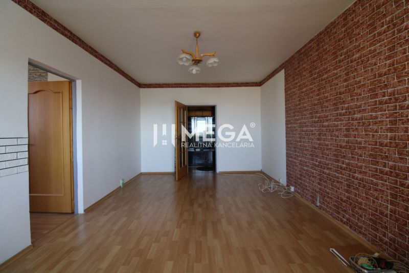 Ein Zimmer in einer 3-Zimmer-Wohnung mit einem Holzboden und einer Wand im Ziegelmuster.