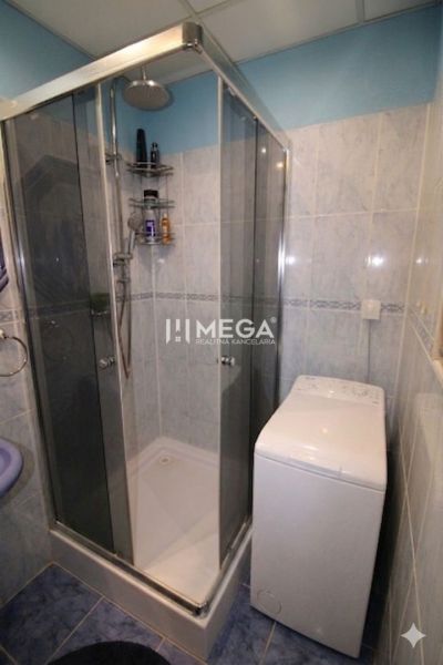 Badezimmer in einer 3-Zimmer-Wohnung mit Fliesen, Duschkabine und Waschmaschine.