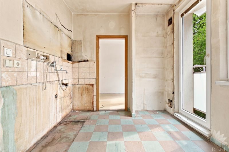 Küche in einer 2-Zimmer-Wohnung ohne Ausstattung, abgenutzte Wände, Blick nach draußen.