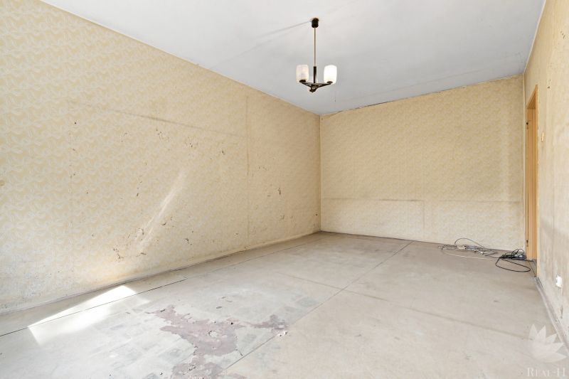 Leerer Raum mit Tapeten, Kronleuchter und beschädigtem Boden in einer 2-Zimmer-Wohnung.