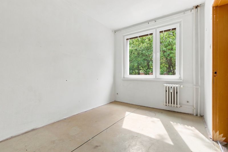 Leerer Raum in einer 2-Zimmer-Wohnung mit großem Fenster und Heizkörper, hellen Wänden.