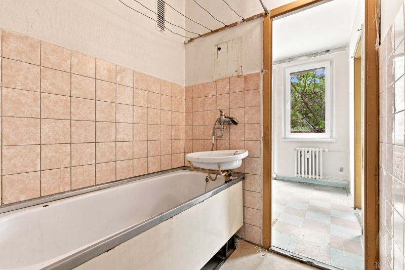 Badezimmer mit Badewanne und Waschbecken, das in einen hellen Raum in einer 2-Zimmer-Wohnung führt.