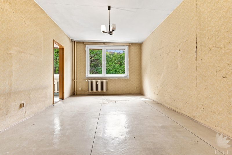 Zimmer in einer 2-Zimmer-Wohnung, beigefarbene Tapeten, großes Fenster, Heizkörper.