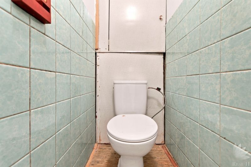 Toilette mit grünen Fliesen in einer 2-Zimmer-Wohnung und einem Boden in Holzoptik.