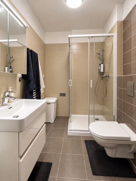 Badezimmer in einer 2-Zimmer-Wohnung mit moderner Duschkabine, eingebautem Waschbecken und hellen Fliesen.