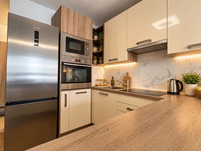 Küche in einer 2-Zimmer-Wohnung mit Küchenzeile und Geräten aus Edelstahl, Boden mit Holzdekor.
