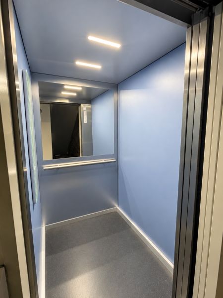 Blaue Aufzugskabine mit Beleuchtung und Spiegel an der Rückwand.
