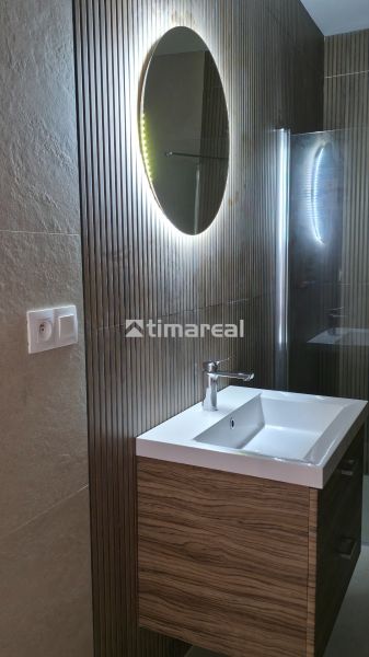 Badezimmer in einem Einfamilienhaus mit beleuchtetem Spiegel und Waschbecken auf einem Schrank mit Holzdekor.