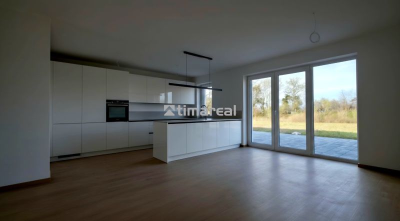 Eine Küche in einem Einfamilienhaus mit einem Boden in Holzoptik und großen Fenstern.