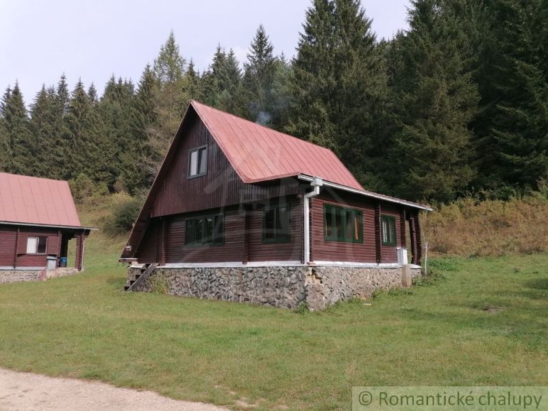 Eine Hütte in Rajecká Lesná mit rotem Dach, Wald und grasbewachsener Umgebung.