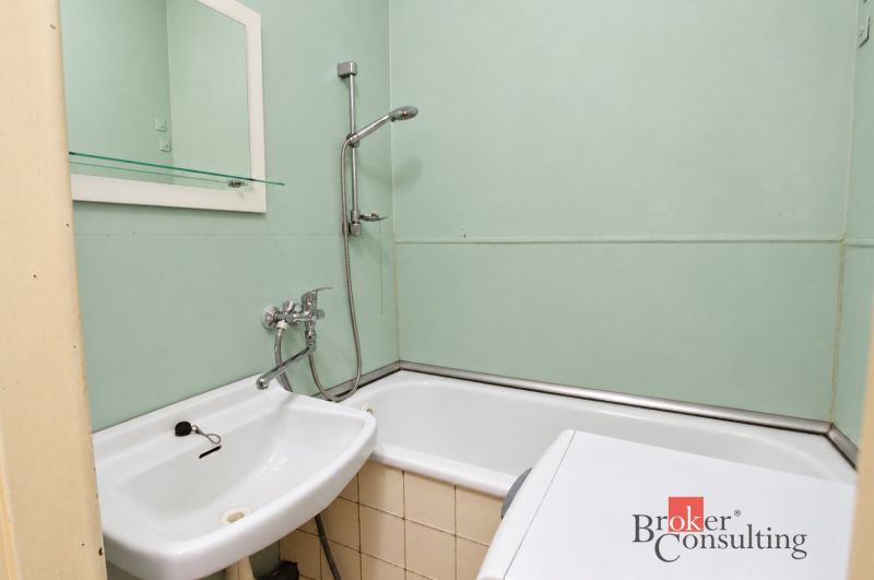 Badezimmer mit Badewanne, weißem Waschbecken, Spiegel und Waschmaschine in einer 2-Zimmer-Wohnung.