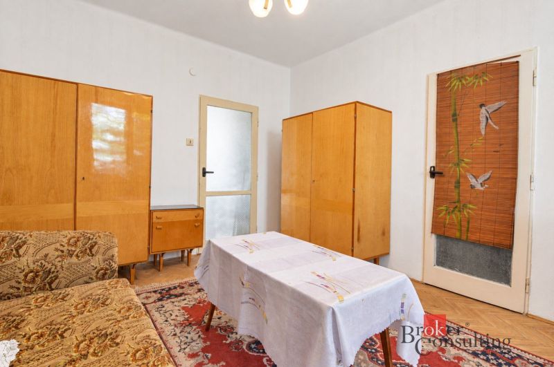 Ein Zimmer in einer 2-Zimmer-Wohnung mit älteren Möbeln und einem Boden in Holzoptik.