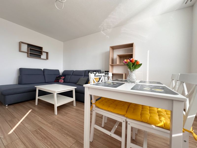 Wohnzimmer mit Ecksofa, weißem Tisch und Boden mit Holzdekor in einer 3-Zimmer-Wohnung.