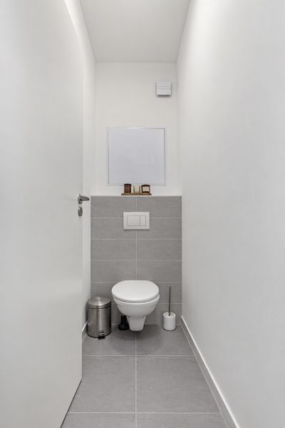 Ein schmales WC mit weißen Wänden und grauen Fliesen in einer Zweizimmerwohnung.