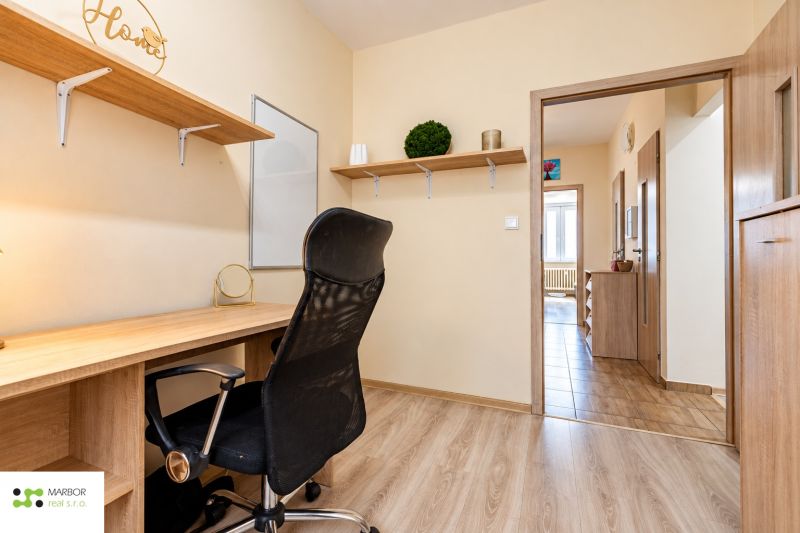 Arbeitsbereich mit Schreibtisch und schwarzem Bürostuhl, ergänzt durch einen Boden mit Holzdekor.