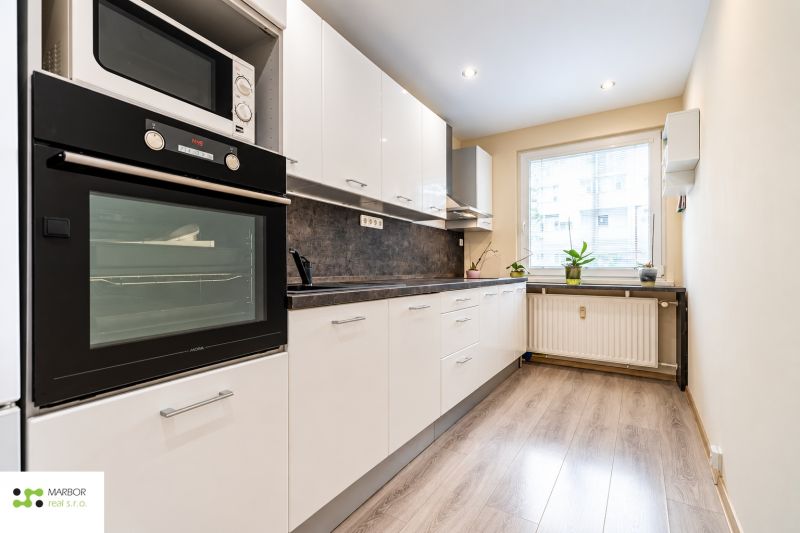 Küche in einer 3-Zimmer-Wohnung mit weißen Schränken und einem Boden in Holzoptik.