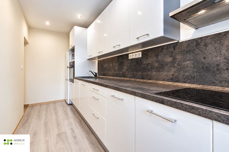 Eine Küche in einer 3-Zimmer-Wohnung mit weißen Möbeln und einem Boden in Holzoptik.