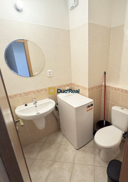 Badezimmer in einem Einzimmerapartment mit Waschbecken, Waschmaschine und Toilette.