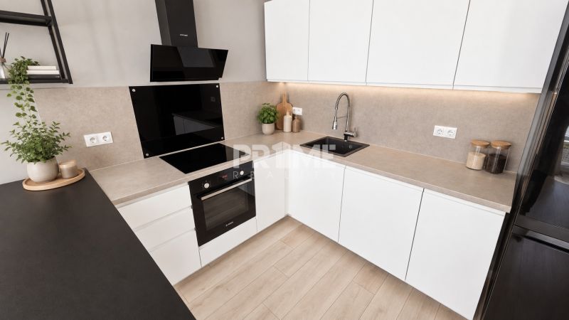 Küche in einer 2-Zimmer-Wohnung mit weißen Schränken, Kochfeld und Holzboden.