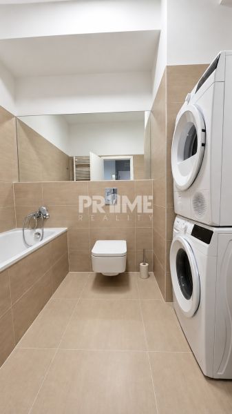 Badezimmer einer 2-Zimmer-Wohnung mit Dusche, Waschmaschine, Trockner und beigen Fliesen.