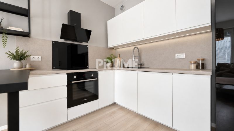 Küche in einer 2-Zimmer-Wohnung mit weißen Schränken und einem Boden in Holzoptik.