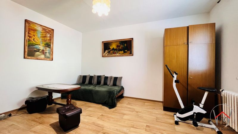 Ein Zimmer in einer 3-Zimmer-Wohnung mit einem Sofa, einem Tisch und einem Boden in Holzoptik.