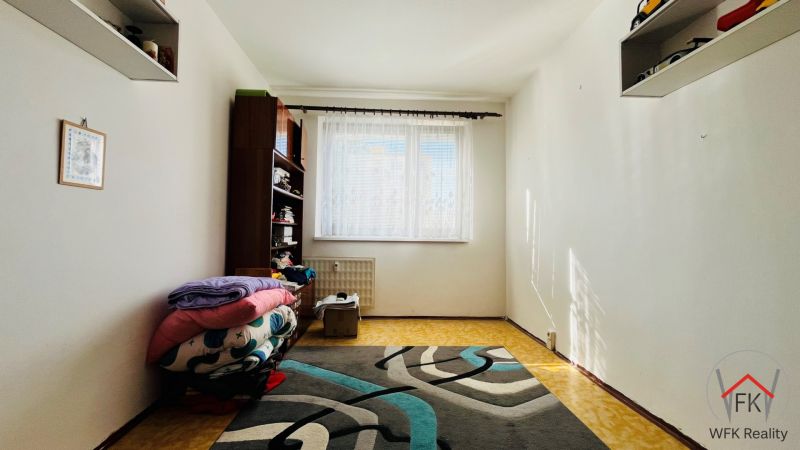 Ein einfaches Zimmer in einer 3-Zimmer-Wohnung mit Teppichboden und einem Regal am Fenster.