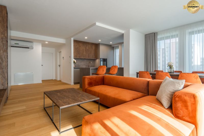 Wohnzimmer mit orangefarbenem Sofa, Küche und Holzboden im Wohnungsbauprojekt.