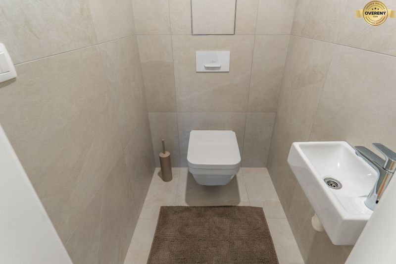 Hänge-WC, kleines Waschbecken und beigefarbene Fliesen im Badezimmer, Wohnungsbau.