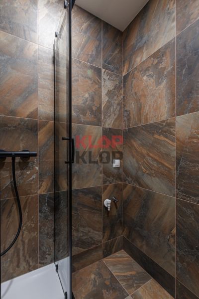 Badezimmer in einer 2-Zimmer-Wohnung mit dunklen Fliesen und einer Glas-Duschwand.