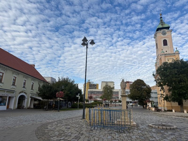 Geschäftsräume in Topoľčany mit einem gepflasterten Platz und einer Kirche im Hintergrund.