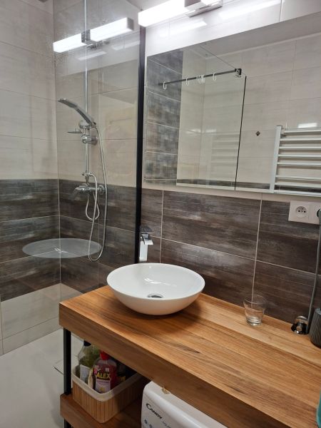 Badezimmer in einer Einzimmerwohnung mit Waschbecken und Dusche, Boden mit Holzdekor.