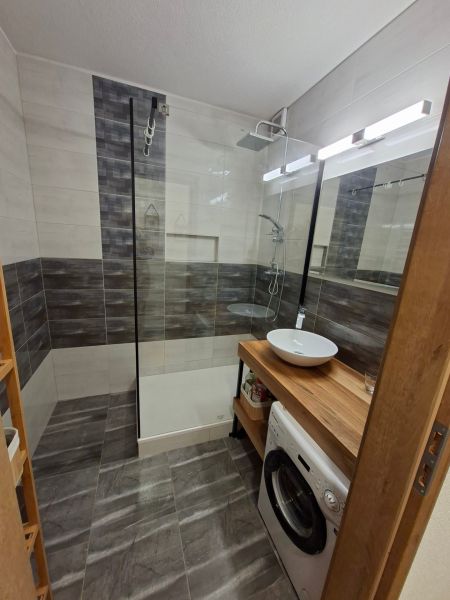 Badezimmer in einer Einzimmerwohnung mit Waschbecken, Duschkabine und Waschmaschine.