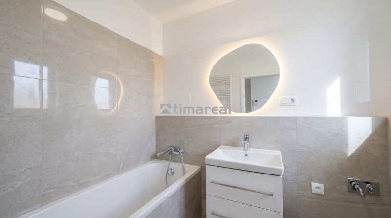 Badezimmer in einer 2-Zimmer-Wohnung mit Badewanne, Waschbecken und beleuchtetem Spiegel.