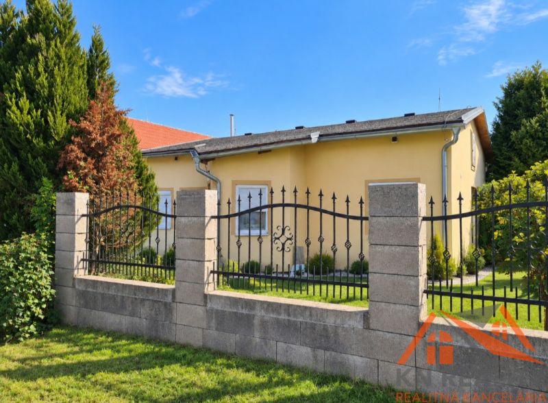 Ein Einfamilienhaus in Martovce mit einem Garten, umgeben von grünen Bäumen und einem Zaun.