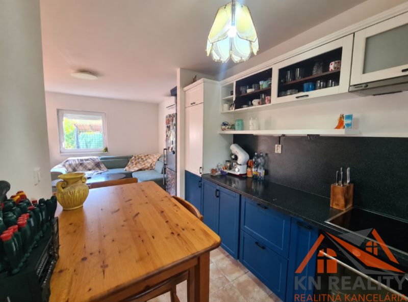 Eine Küche in einem Einfamilienhaus mit einem Holztisch, blauen Schränken und einem Sofa im Hintergrund.