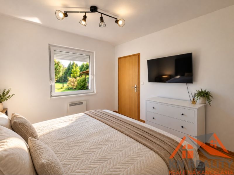 Ein Schlafzimmer in einem Einfamilienhaus mit hellen Möbeln, einem Fenster und einem Fernseher an der Wand.