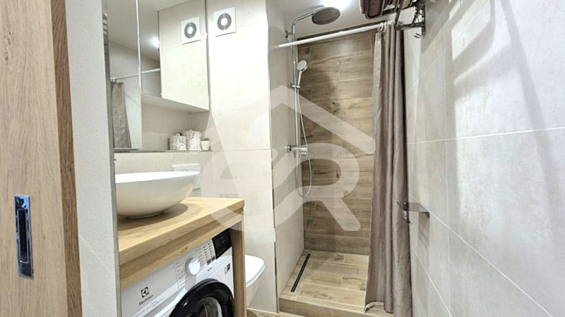 Badezimmer in einem Studio-Apartment mit Holzboden, Dusche und Waschmaschine.