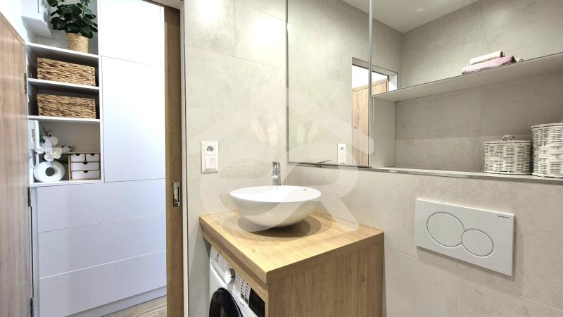 Badezimmer in einem Studio-Apartment mit weißem Waschbecken, Holzdekor und Aufbewahrungskörben.