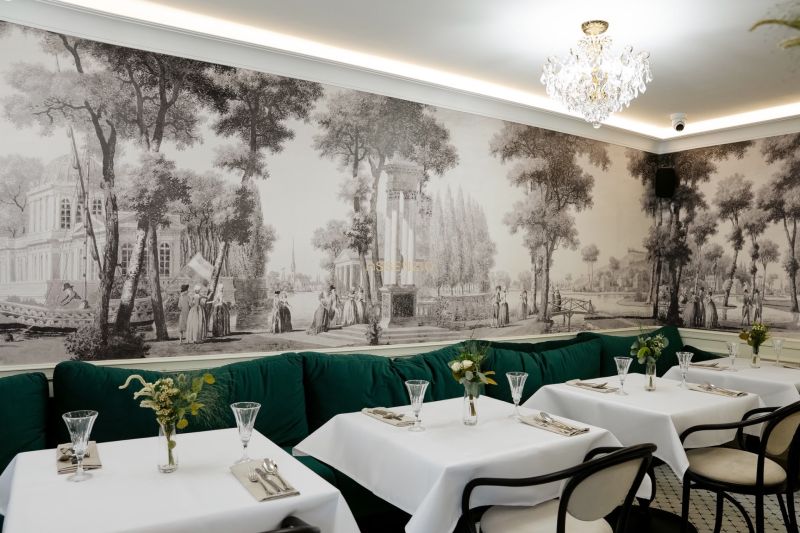 Ein Restaurant mit historischer Tapete, Kristallleuchter und grünen Sitzbänken in Geschäftsräumen.
