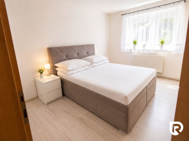 Schlafzimmer mit Bett, Nachttischen und Boden mit Holzdekor in einer 2-Zimmer-Wohnung.