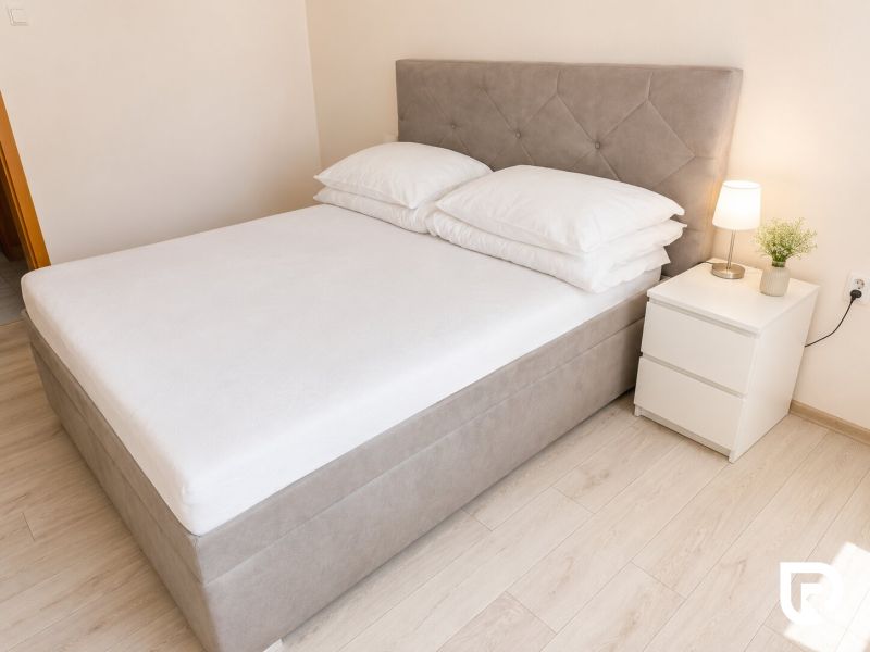 Bett mit Nachttisch und Lampe in einer 2-Zimmer-Wohnung auf einem Boden mit Holzdekor.