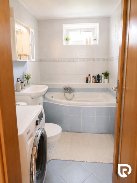Badezimmer in einer 2-Zimmer-Wohnung mit Badewanne, Waschmaschine und Fliesen in hellem Farbton.