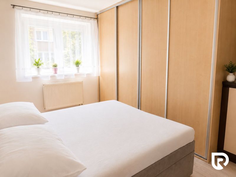 Schlafzimmer in einer 2-Zimmer-Wohnung mit Bett, Schränken und einem Fenster mit Pflanzen.